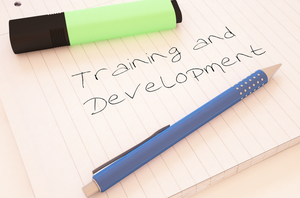 Lined notebook page with handwritten text that reads Training and Development. A blue pen rests diagonally across the page and a green highlighter lies above the text.