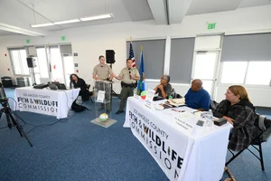 A group of people sitting at tables at an event while 2 officers speaks to them.