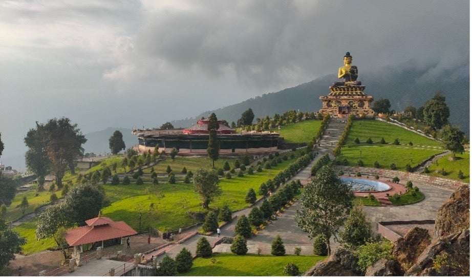 A rolling hill with a giant buddha statue on top stands against a foggy sky in India. 
