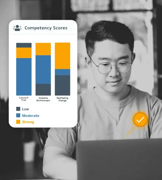 Youthful business professional man in a t-shirt and wearing wire-framed glasses while sitting at a laptop and implementing insights from DDI assessments. A graphically designed box features a vertical bar chart with the heading "Competency Scores."