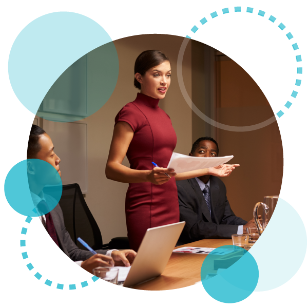 confident woman leader standing in a board room holding papers and a pen surrounded by two of her colleagues who are sitting?fm=webp&q=65