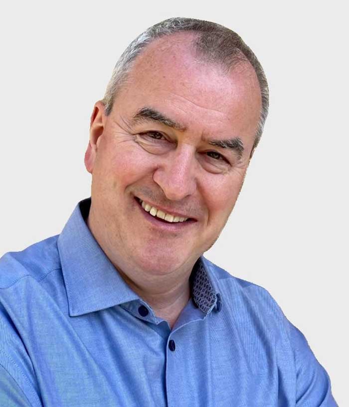 Kenny Simmen, a man with graying dark hair, wears a blue button down shirt.