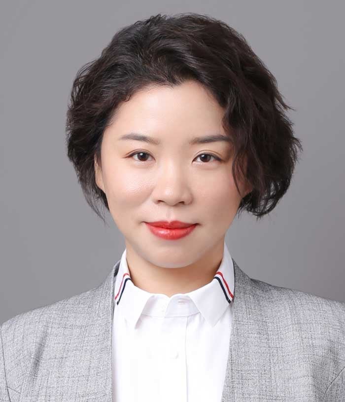 Ninie Wang, a woman with black hair, wears a gray blazer and a white collared shirt with vertical red, white, and blue stripes on either side.