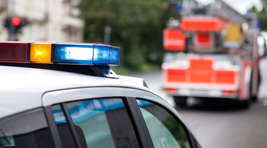 Close-up of a police car's light bar with a fire truck in the background.