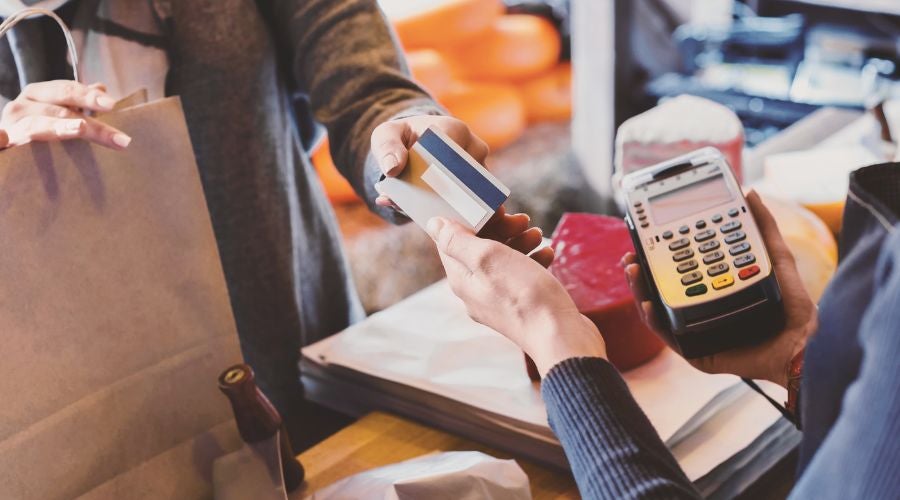 A person handing a payment card to another person at a checkout counter.
