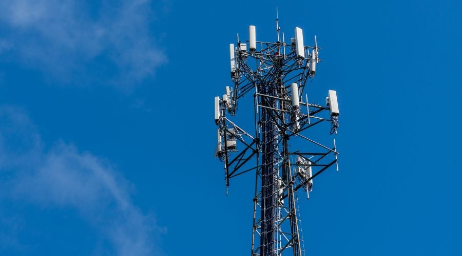 Cell tower with multiple antennas against a blue sky.
