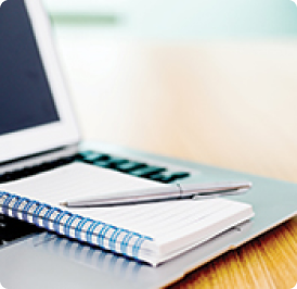A laptop with a notebook and pen on a wooden table.