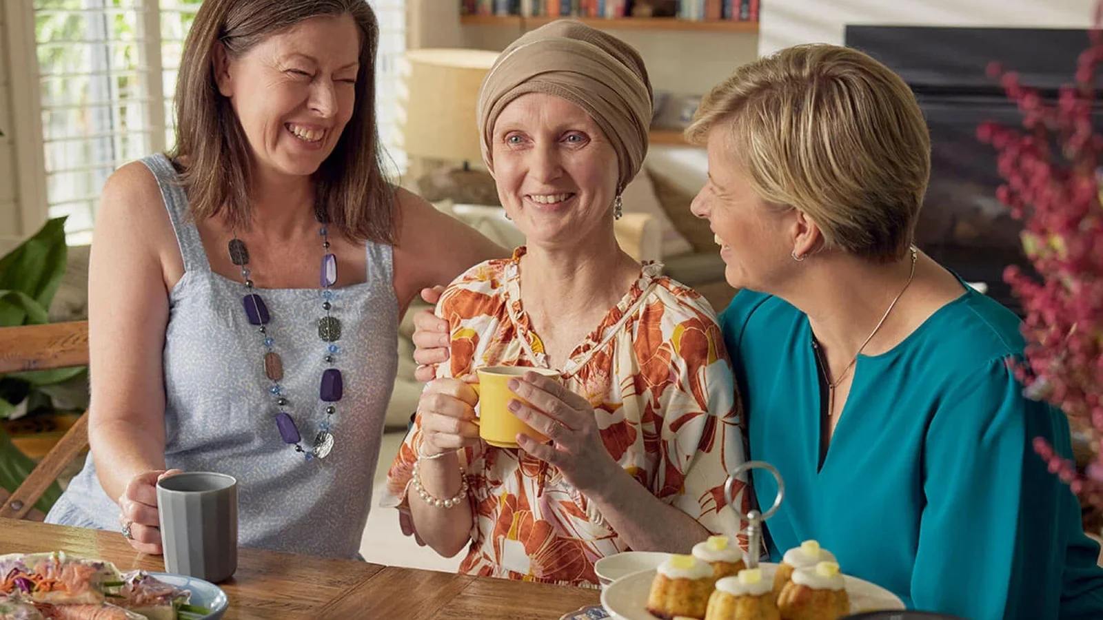 Three women laughing, the one in the middle wearing a scarf on her head. 