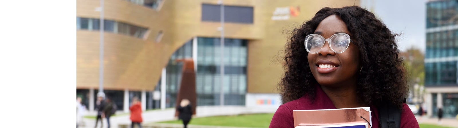 Student smiling and holding books outside Teesside campus