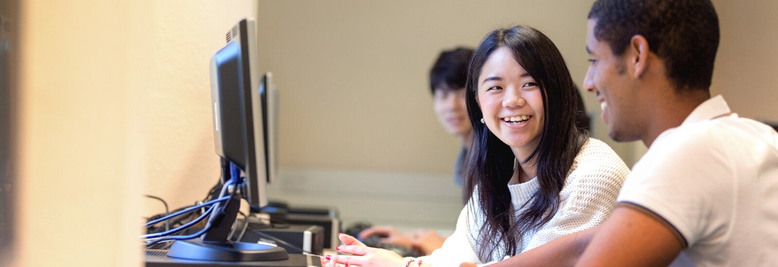Two students working on computers and laughing