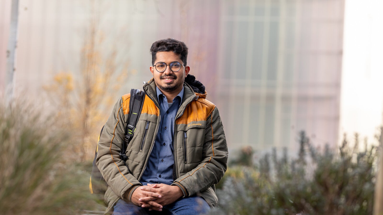 Student smiling and sitting on a wall outside campus