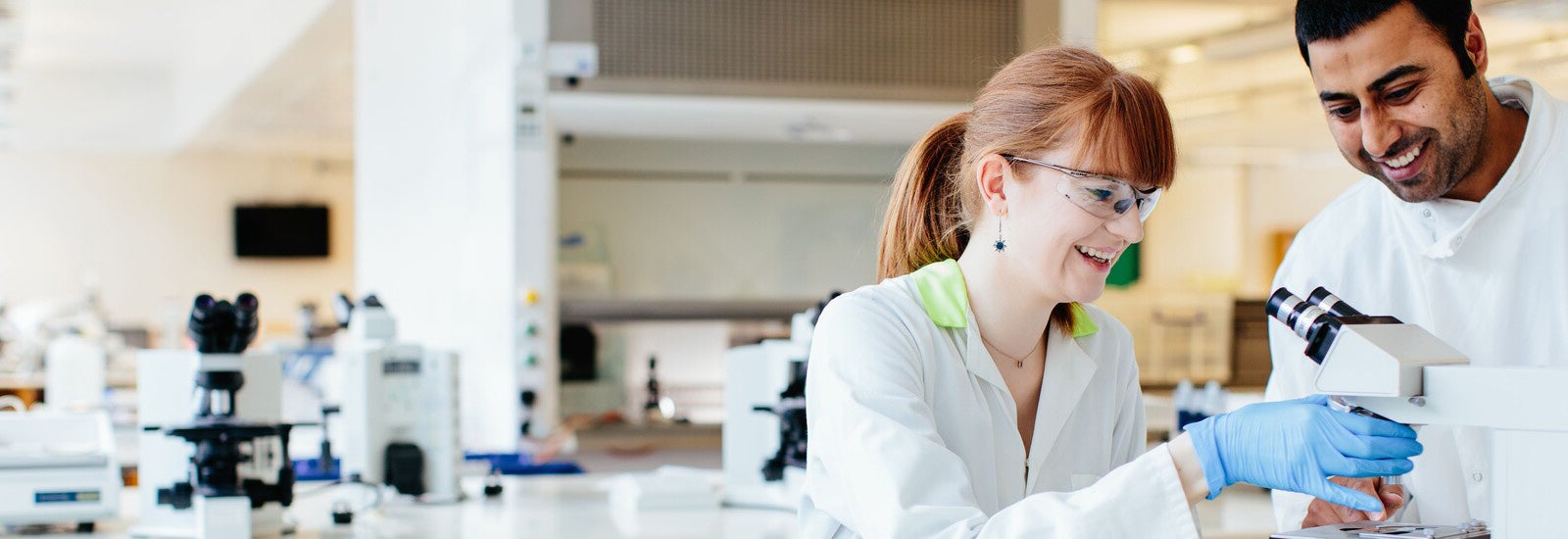 Two smiling students in a lab using a microscope