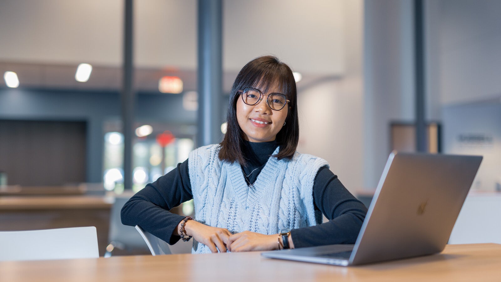 A student smiling at a desk with a laptop