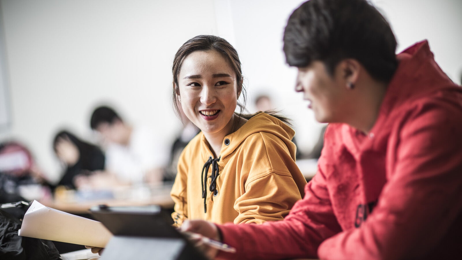 Two students smiling with each other in class, using an iPad