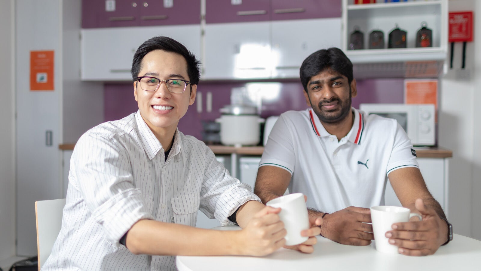 Two students holding mugs and smiling at a kitchen table