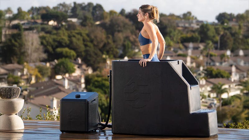 A woman in athletic attire standing in an Ice Barrel cold plunge tub with a play button overlaid on the image