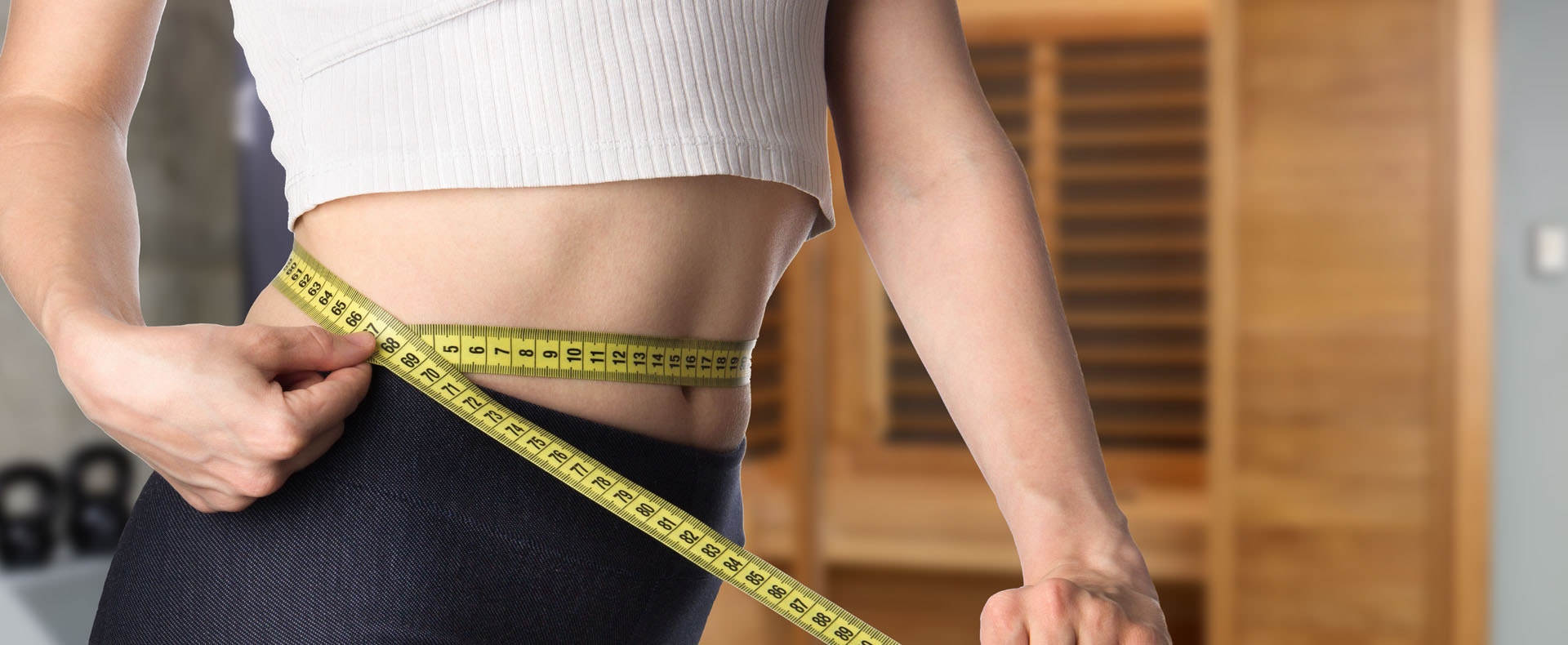 A fit person measuring their waist with a tape measure.
