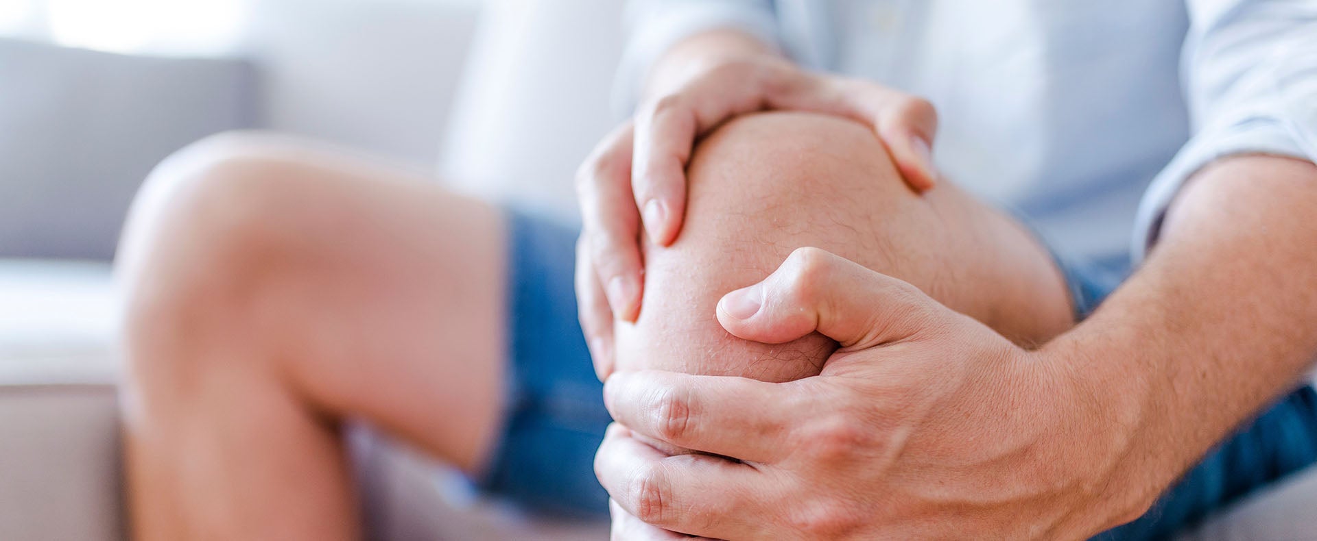 A person seated, holding their knee and leg muscles in pain. 