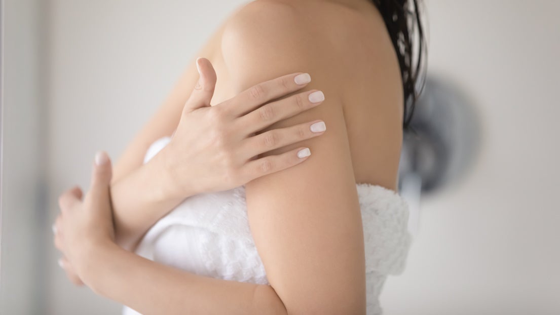 A woman with smooth skin rubs her shoulder.