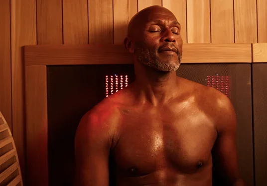 Older man relaxing with eyes closed inside a Sunlighten infrared sauna, basking in red light therapy for cardiovascular and stress relief benefits.