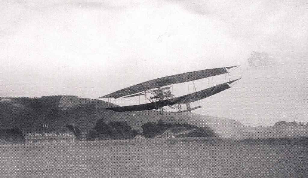 Glenn Curtiss piloting the Aerial Experiment Association’s June Bug, July 4, 1908. Note the triangular ailerns at the ends of each set of wings. House, Kirk W. Hell-rider to King of the Air: Glenn Curtiss’s Life of Innovation. SAE International, 2003. View Source.