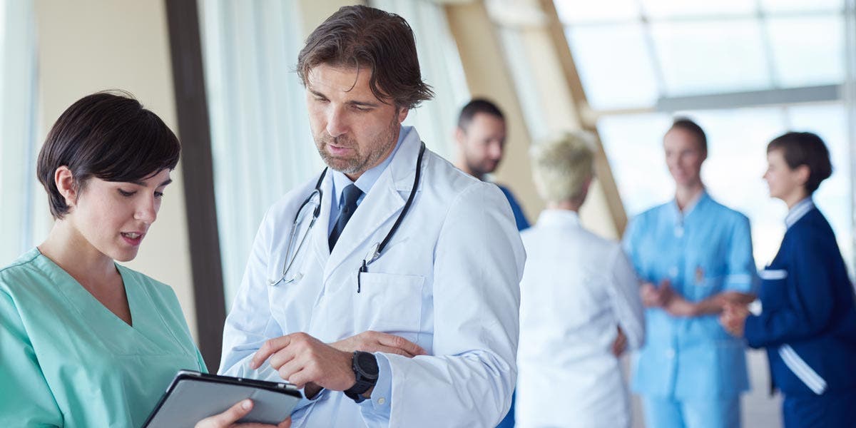Photo representing culture change happening in healthcare with doctor and nurse having a discussion over a clipboard as colleagues chat in the background