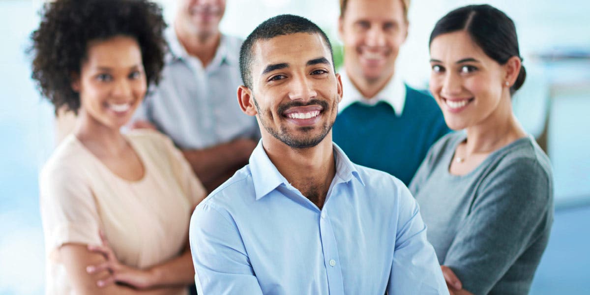 team of highly engaged employees standing in a group, all smiling, with a young man leader standing at the front of the group confident and happy he has been developed as a leader with the skills to positively impact engagement and retention on his team