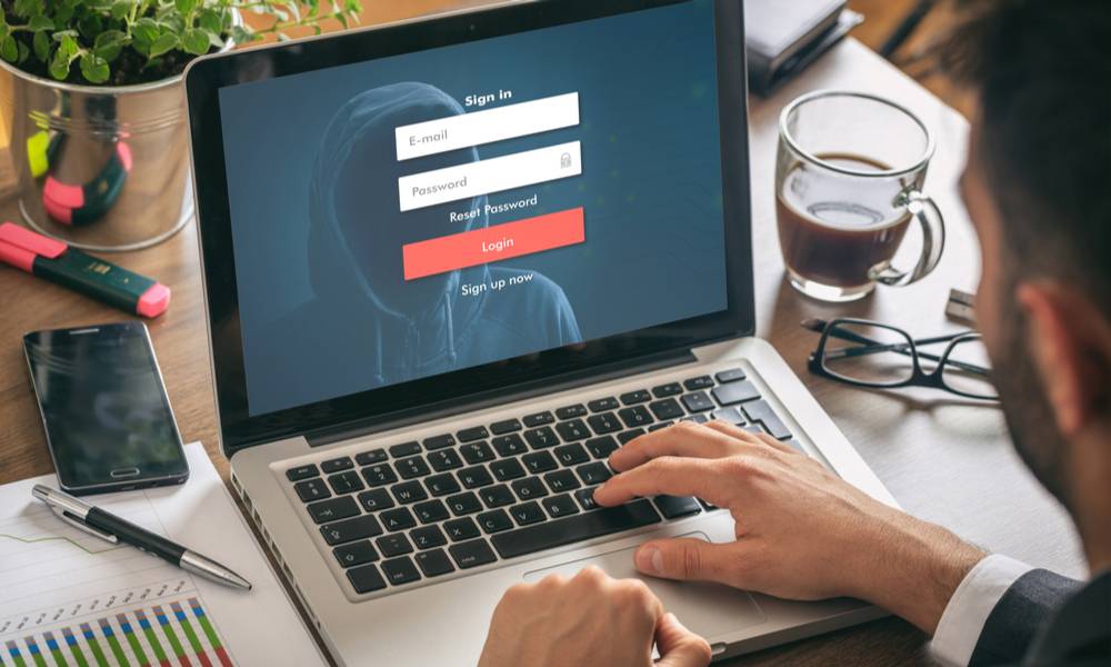 Businessman clicks on sign in page appears on screen reflecting a hooded hacker (1).jpg