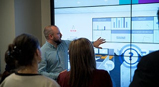 man stood in front of a group touching an interactive board