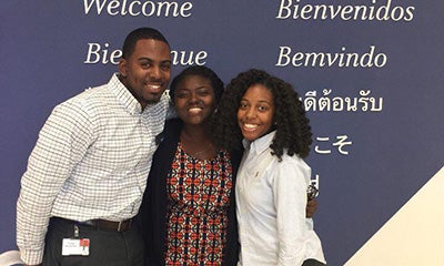 two women and a man smiling in front of a welcome sign