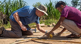 two males knelt down making something out of bamboo