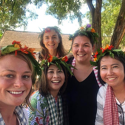 vijf vrouwen met bloemversieringen op hun hoofd glimlachen naar de camera