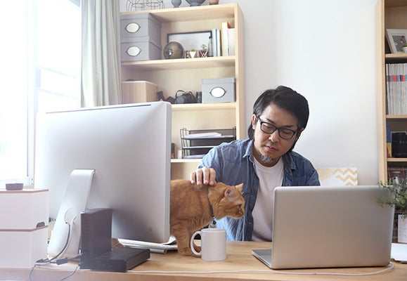 a man sat at a desk whilst stroking his cat on the desk