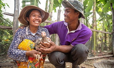 man and woman smiling and hugging knelt down whilst the woman is holding a chicken