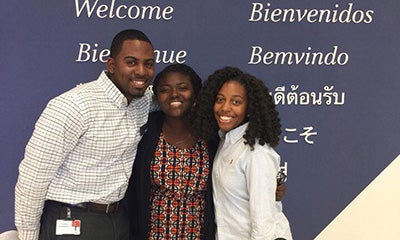 two women and a male smiling in front of a welcome sign