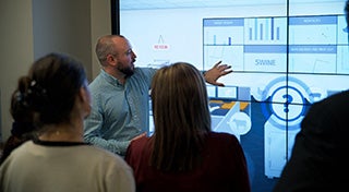 man stood in front of a group pointing at a interactive board