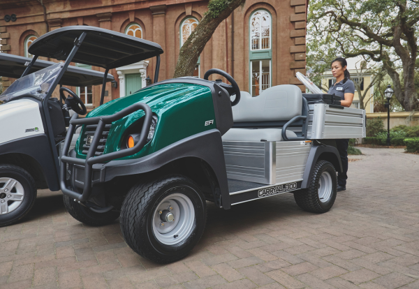 A woman carries equipment to a Club Car Carryall on a university campus.