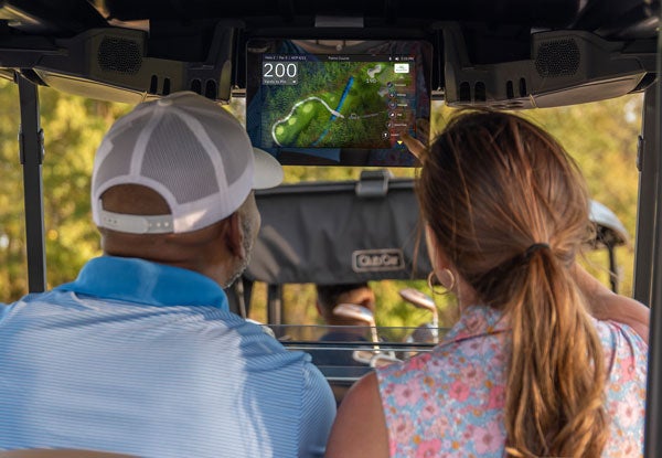 Two people sitting in a golf cart look at their Club Car Connect monitor.