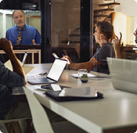 A group meeting with four people at a table and a presenter on a screen.