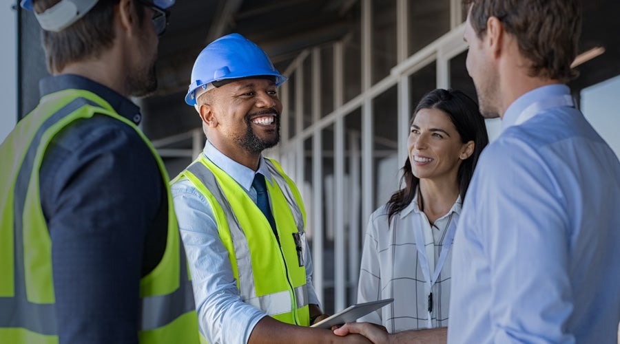 Construction contractor in a safety vest and hard hat shaking hands with a business professional at a job site, joined by team members from Chatsworth Products.