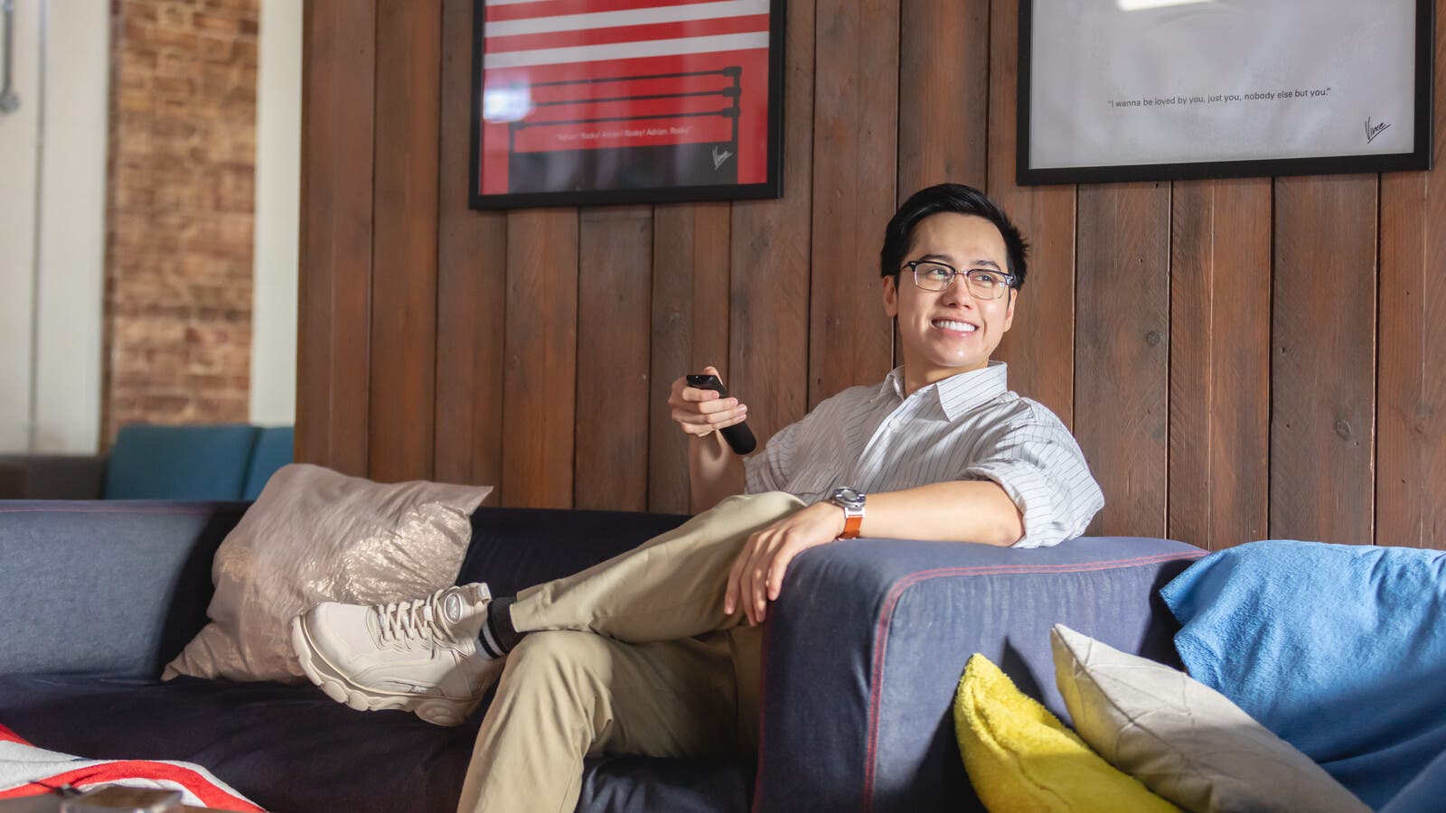 A smiling student sitting back on a sofa holding a remote