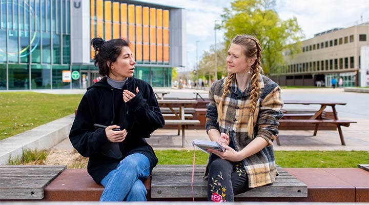 Students sitting on bench outside campus