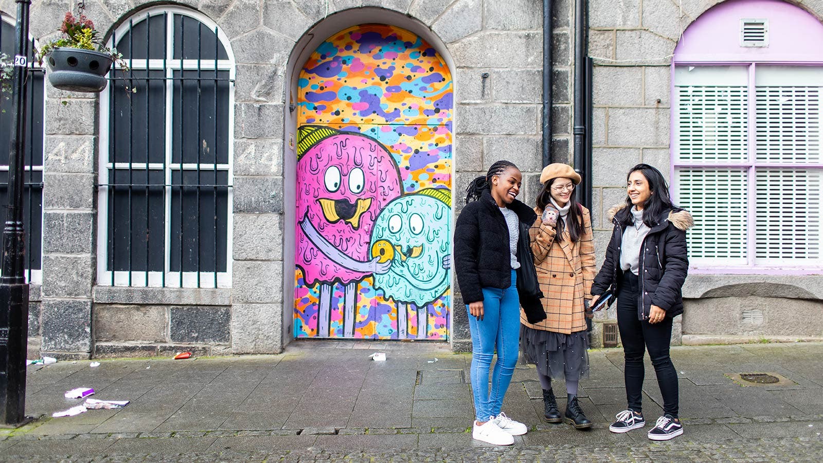 Three students in front of street art.