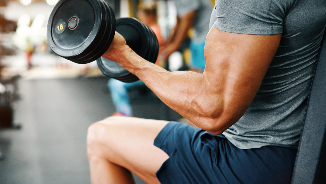 A man in a gym lifts a weight. 