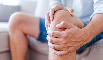 A person seated, holding their knee and leg muscles in pain.