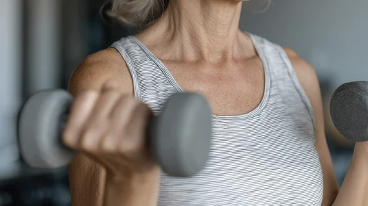 Close-up of a fit older woman lifting dumbbells during a strength training workout, supporting longevity and muscle health.