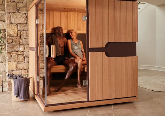 Happy couple sitting together inside a Sunlighten infrared sauna, sharing a relaxing and health-boosting experience.
