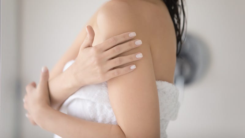 A woman with smooth skin rubs her shoulder.
