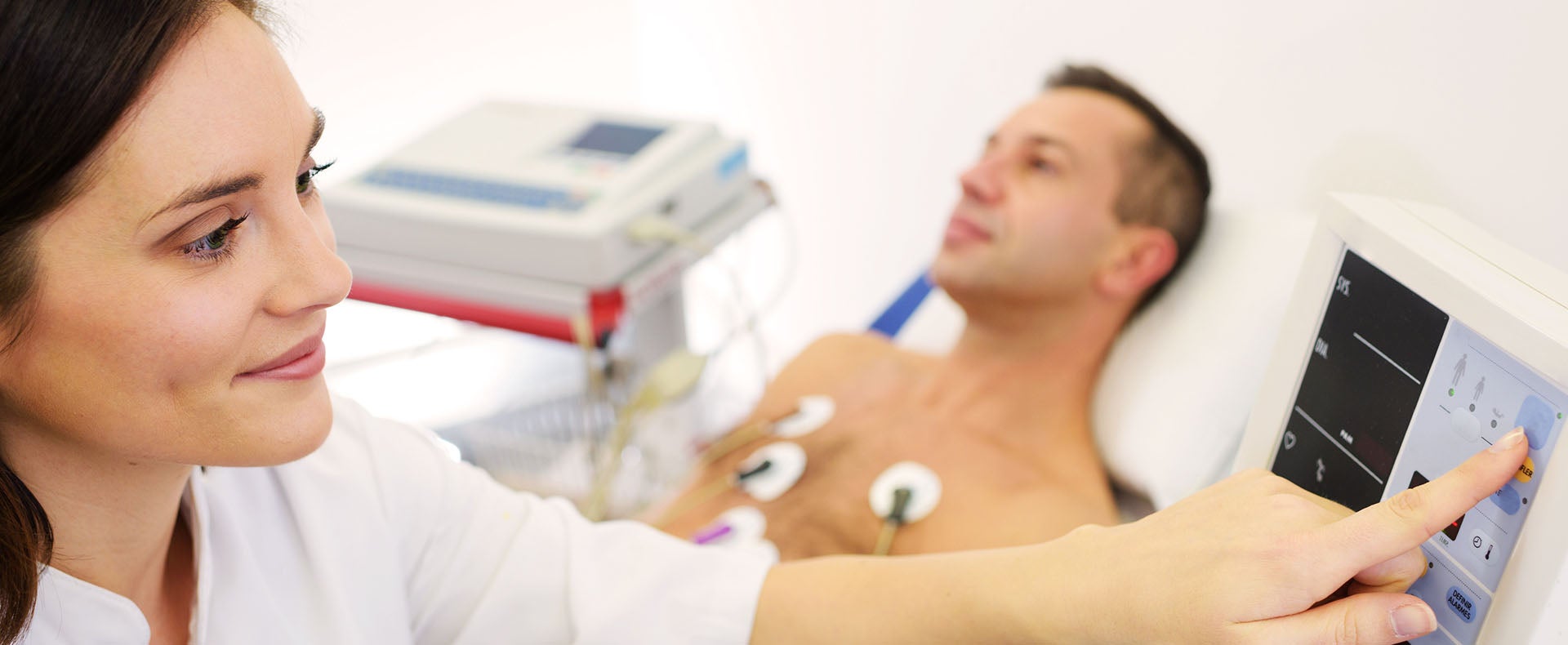 A doctor monitors the vital signs of a patient fitted with electrodes and a heart monitor.