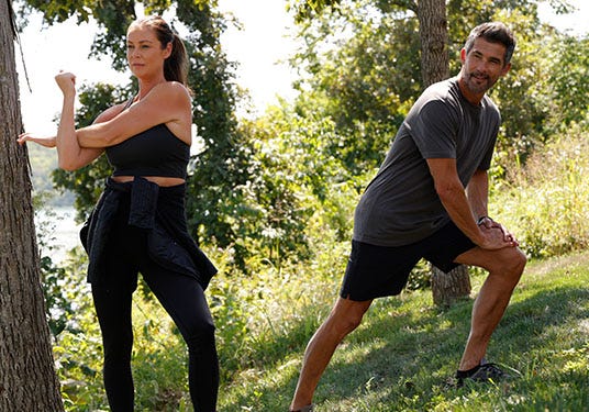 A man and woman stretch on a grassy hill.